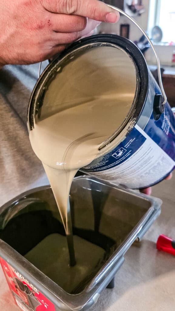 Pouring interior cabinet paint into a paint tray before applying the first coat to a primed kitchen island during a DIY kitchen makeover.