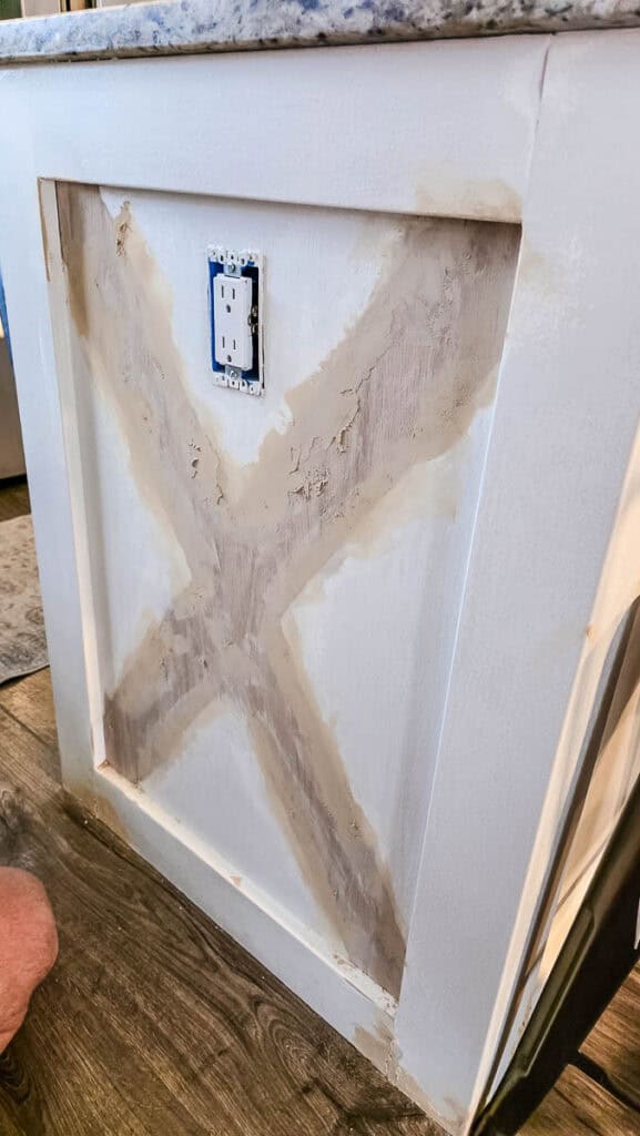Kitchen island after sanding and wood filler application, showing repaired decorative X-pattern trim and patched imperfections before priming and painting.
