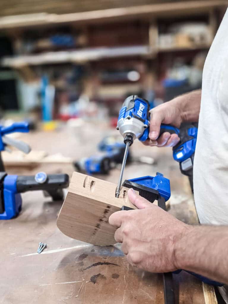 A woodworker uses a cordless impact driver to assemble a wooden napkin holder, fastening the side panels together during a DIY woodworking project.