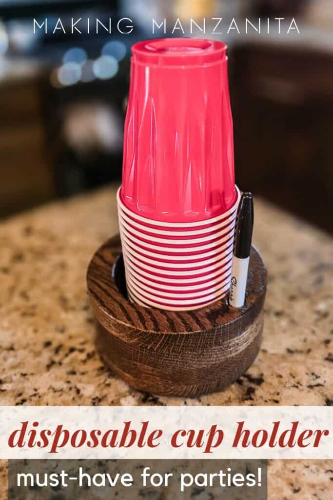 Dark stained wooden disposable cup holder with a built-in marker slot, holding a stack of red plastic party cups on a granite countertop. Text reads, "Disposable cup holder – must-have for parties!"