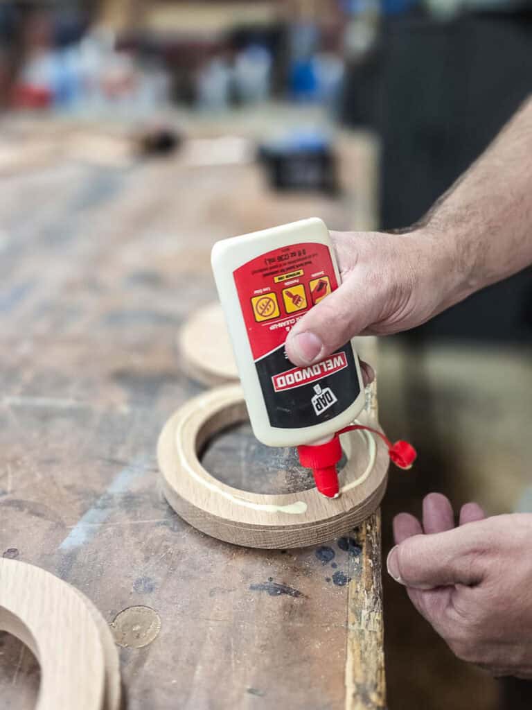 Wood glue is applied to a circular wooden cup holder ring during assembly of a DIY wooden holder for disposable cups and napkins.