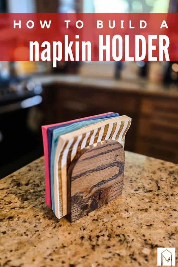 DIY wooden napkin holder made from dark-stained wood, holding colorful paper napkins on a granite kitchen countertop. Text at the top reads, "How to Build a Napkin Holder."