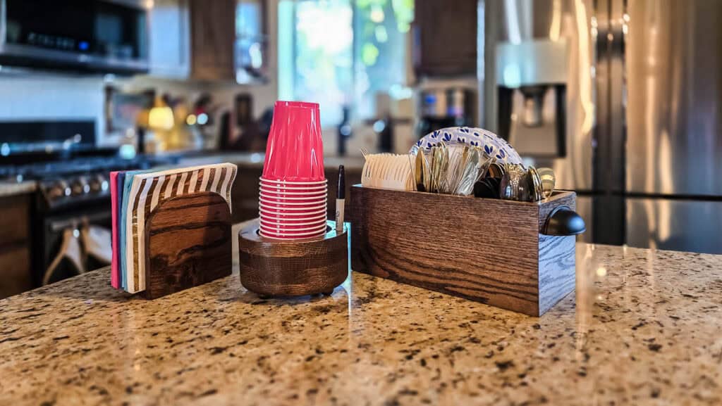 DIY wooden cup holder, napkin holder, and utensil caddy displayed together on a kitchen countertop.